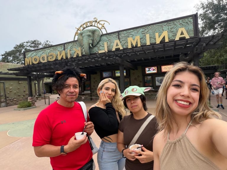 Four friends smiling for a selfie in front of a vintage carousel building at an amusement park