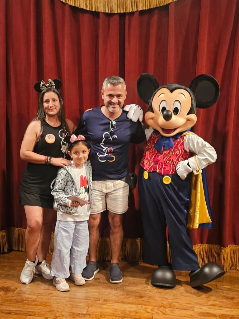Family posing with Mickey Mouse character in front of red velvet curtain at Disney attraction