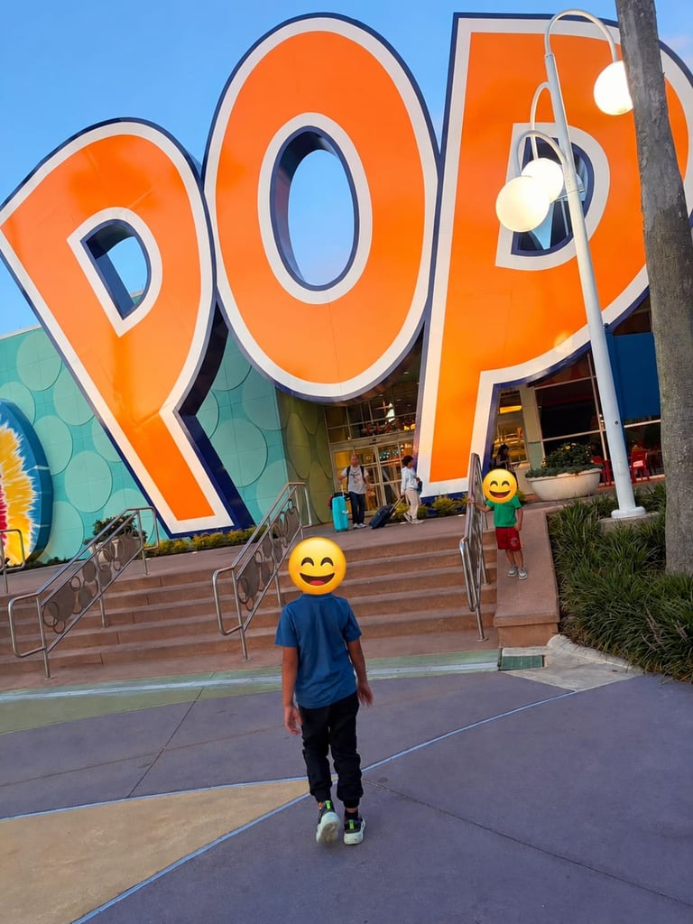 Person in blue shirt standing in front of large orange POP sign at outdoor venue with stairs and storefronts visible